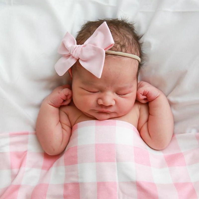 Sleeping newborn under a pink gingham swaddle blanket